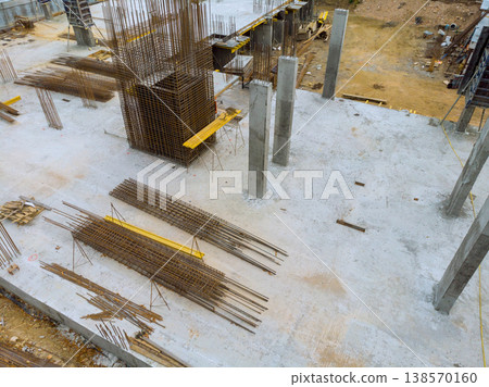 Construction site features concrete pillars being set with steel reinforcement bars placed on ground. Construction site features concrete pillars being set with steel reinforcement bars placed on ground. 138570160