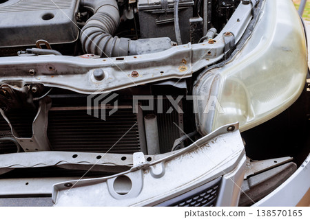 Mechanic works on car parts in service garage engine hood is open tools are scattered around. 138570165