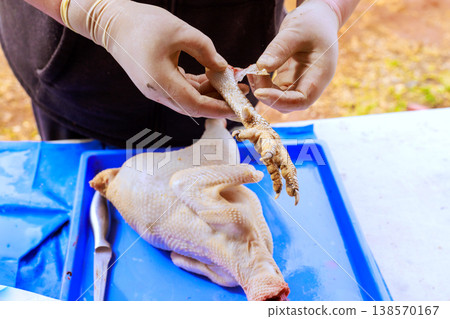 Butcher uses gloves to peel skin off chicken feet at market stand during food preparation. 138570167