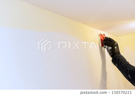 Carpenter using tool to smooth paint on wall in home wall shows two colors of paint. Carpenter using tool to smooth paint on wall in home wall shows two colors of paint. 138570221