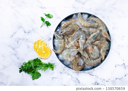 Fresh raw shrimp spread on ice with lemon and cilantro slices on a marble surface, ready to cook, no people Fresh raw shrimp spread on ice with lemon and cilantro slices on a marble surface, ready to cook, no people 138570659