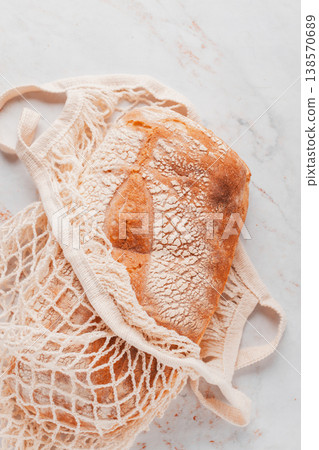 freshly baked rye bread, ciabatta, in a mesh bag, on a marble light table, natural light, 138570689