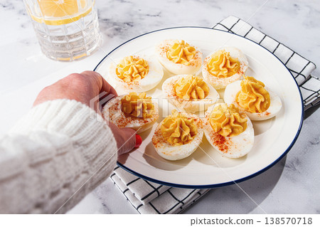 stuffed eggs with paprika, on a plate, a woman's hand reaches for it, stuffed eggs with paprika, on a plate, a woman's hand reaches for it, 138570718