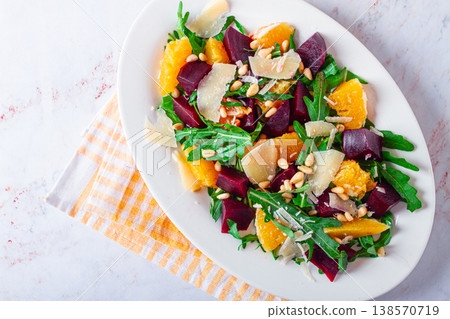 Fresh salad with beets, oranges, and arugula topped with cheese and nuts served on a white plate Fresh salad with beets, oranges, and arugula topped with cheese and nuts served on a white plate 138570719
