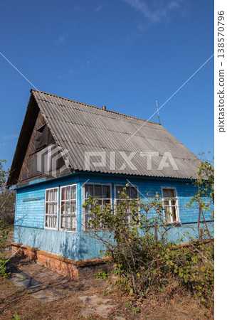 A small wooden village country house with a triangular roof. An old hut with a garden plot. 138570796