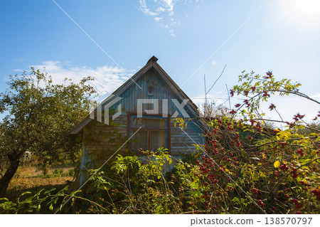 A small wooden village country house with a triangular roof. An old hut with a garden plot. A small wooden village country house with a triangular roof. An old hut with a garden plot. 138570797