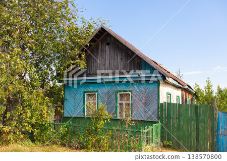 A blue and green house with a wooden fence. The house has a slanted roof and a porch A blue and green house with a wooden fence. The house has a slanted roof and a porch 138570800