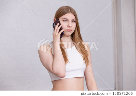 Young woman stands while talking on a smartphone in a bright indoor space during a casual day Young woman stands while talking on a smartphone in a bright indoor space during a casual day 138571266