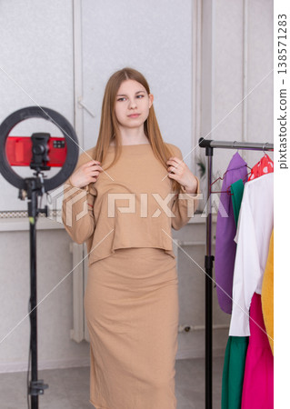 Model poses in stylish beige outfit for fashion shoot in studio with colorful clothing rack Model poses in stylish beige outfit for fashion shoot in studio with colorful clothing rack 138571283