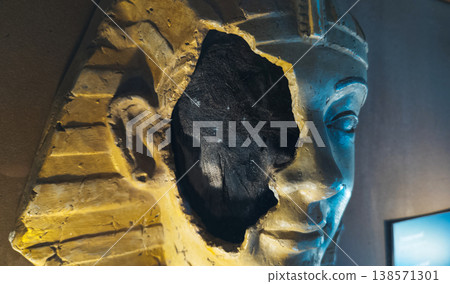 Ancient egyptian pharaoh mask or mummy head exhibit in a museum, featuring a broken face detail with visible inner layers, golden textures, and dramatic lighting. Ancient egyptian pharaoh mask or mummy head exhibit in a museum, featuring a broken face detail with visible inner layers, golden textures, and dramatic lighting. 138571301