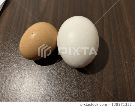 Comparison of natural farm fresh brown egg and industrially produced perfect white egg on dark wood contrast Comparison of natural farm fresh brown egg and industrially produced perfect white egg on dark wood contrast 138571332