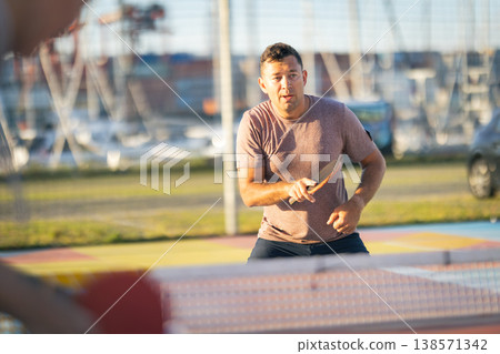 Man playing table tennis outdoors concentrating on game Man playing table tennis outdoors concentrating on game 138571342