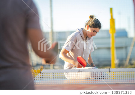 Woman playing table tennis against opponent outdoors Woman playing table tennis against opponent outdoors 138571353