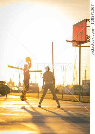 Young men playing basketball jumping for a shot at sunset Young men playing basketball jumping for a shot at sunset 138571367