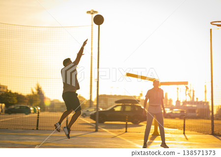 Young people playing basketball jumping shooting ball during sunset Young people playing basketball jumping shooting ball during sunset 138571373