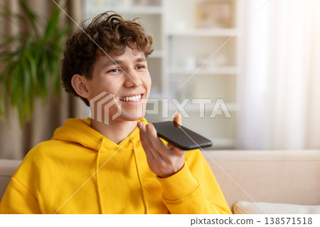Young smiling teen guy in yellow hoodie holding phone in speakerphone mode 138571518
