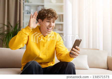 Excited teen guy waving hand at smartphone screen during video call Excited teen guy waving hand at smartphone screen during video call 138571573