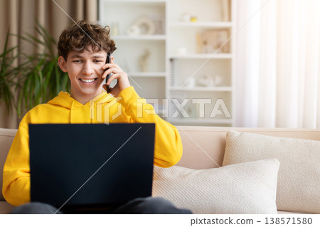 Happy teen boy talking on phone while using laptop at home Happy teen boy talking on phone while using laptop at home 138571580