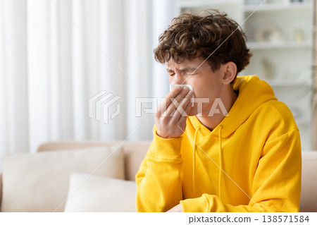 Sick teen boy blowing nose with tissue, sitting on sofa at home 138571584