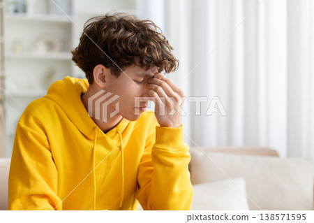 Stressed teen guy suffering headache, pressing fingers to forehead with eyes closed Stressed teen guy suffering headache, pressing fingers to forehead with eyes closed 138571595