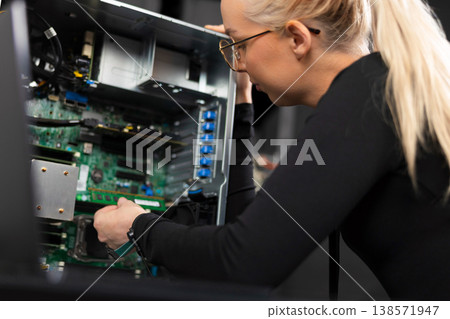 Female IT technician upgrades and repairs server hardware in a data center, focused on diagnostics and maintenance Female IT technician upgrades and repairs server hardware in a data center, focused on diagnostics and maintenance 138571947