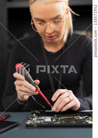 Female IT technician in her twenties repairs a laptop with precision screwdriver Female IT technician in her twenties repairs a laptop with precision screwdriver 138571952
