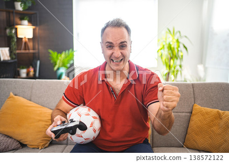 Middle age Caucasian man playing soccer video game at home Middle age Caucasian man playing soccer video game at home 138572122