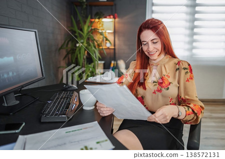 Smiling businesswoman reviewing documents at her home office desk Smiling businesswoman reviewing documents at her home office desk 138572131