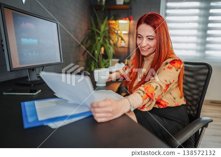 Businesswoman smiling while reading documents at her desk 138572132