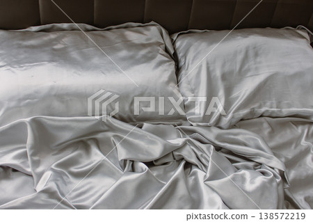 Grey silk sheet on a bed. Luxury bed linen. Hotel bedroom concept. Comfortable bed with fabric and two pillows. Double bed for couple. Rumpled bedding after sleeping. Two pillows on the sofa. 138572219