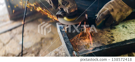Worker wearing protective gloves using an angle grinder to cut or grind a metal workpiece, creating numerous bright sparks and demonstrating industrial craftsmanship. Worker wearing protective gloves using an angle grinder to cut or grind a metal workpiece, creating numerous bright sparks and demonstrating industrial craftsmanship. 138572418