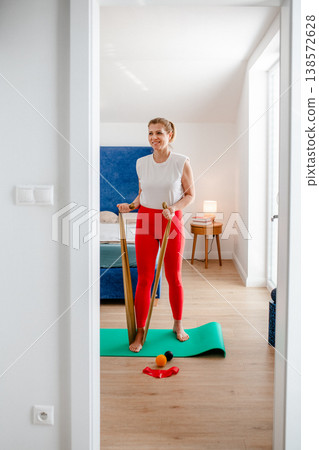 Smiling middle aged woman exercising with resistance band at home. Smiling middle aged woman exercising with resistance band at home. 138572628