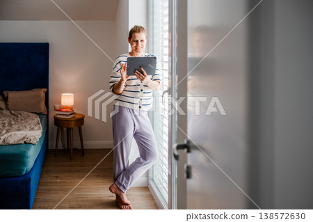 Woman using tablet at home near window in morning light. Woman using tablet at home near window in morning light. 138572630