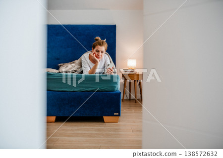 Middle aged woman using smartphone while lying in bed at home. Middle aged woman using smartphone while lying in bed at home. 138572632