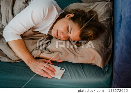 Tired middle aged woman sleeping in bed after using smartphone. Tired middle aged woman sleeping in bed after using smartphone. 138572633