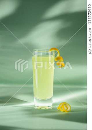 Limoncello Glasses with Curled Lemon Peels on Light Green Background. Limoncello Glasses with Curled Lemon Peels on Light Green Background. 138572650