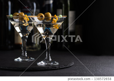 Two martini glasses with skewered green olives and citrus twists against dark background Two martini glasses with skewered green olives and citrus twists against dark background 138572658