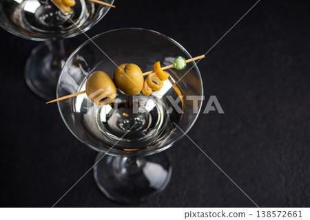 Two martini glasses with skewered green olives and citrus twists against dark background. Two martini glasses with skewered green olives and citrus twists against dark background. 138572661