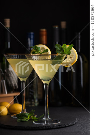 Elegant cocktail two glasses of limoncello spritz, garnished with fresh lemon slices and mint sprigs against a refined bar background with cocktail tools. Elegant cocktail two glasses of limoncello spritz, garnished with fresh lemon slices and mint sprigs against a refined bar background with cocktail tools. 138572664