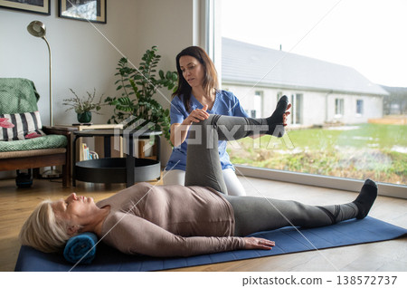 Physiotherapist exercising with senior woman on gym mat. 138572737