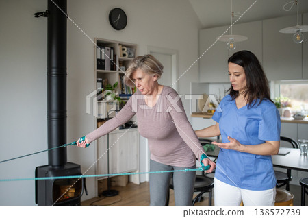 Physiotherapist guiding senior woman during resistance band exercise. Physiotherapist guiding senior woman during resistance band exercise. 138572739