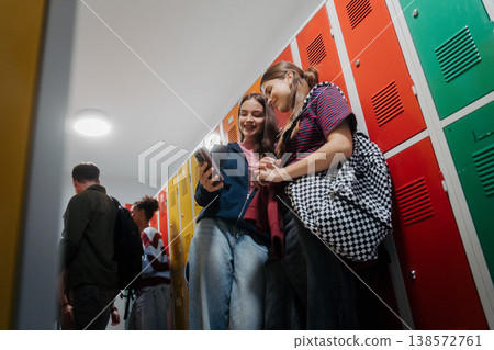 Teen students looing at phone in school hallway by lockers. Teen students looing at phone in school hallway by lockers. 138572761