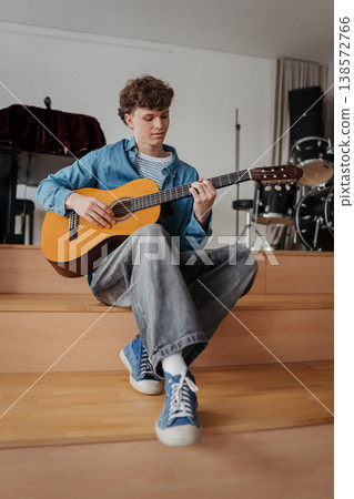 Teenage boy playing acoustic guitar in school music room. Teenage boy playing acoustic guitar in school music room. 138572766