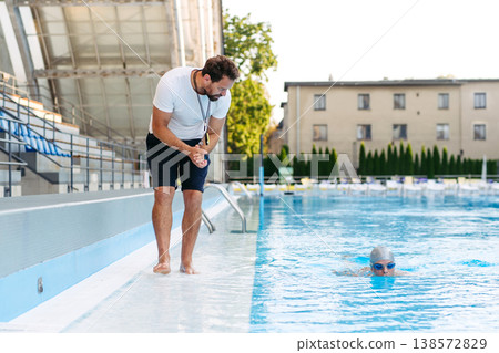 Coach giving advice to young swimme in water, standing by pool. 138572829