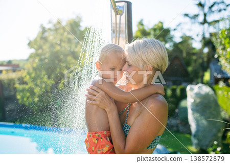 Mother showering under outdoor shower with little son. Mother showering under outdoor shower with little son. 138572879