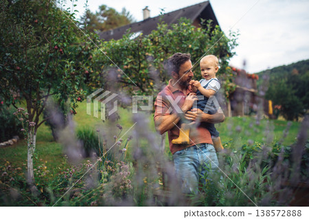 Father holding baby daughter while spending time together in garden. Father holding baby daughter while spending time together in garden. 138572888