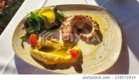 A fried octopus ring with a delicate puree, fresh lettuce leaves, a lemon wedge A fried octopus ring with a delicate puree, fresh lettuce leaves, a lemon wedge 138572914