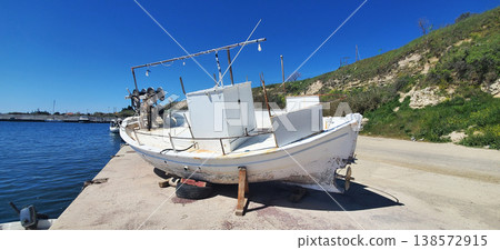 A small fishing boat sits on a concrete dock beside calm blue water. 138572915