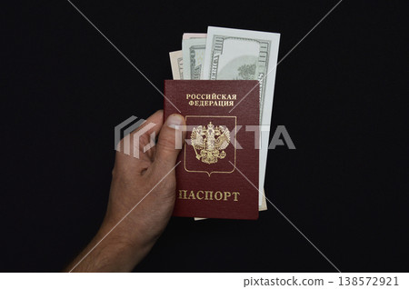Russian passport and invested dollars in a man's hand on a black background Russian passport and invested dollars in a man's hand on a black background 138572921
