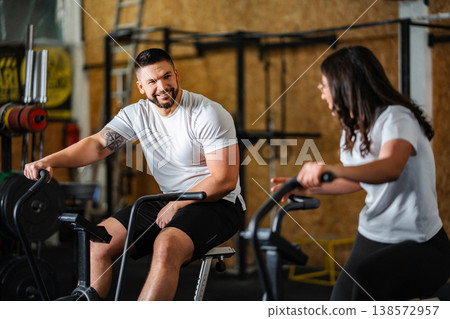 Happy couple working out together on air bikes in gym Happy couple working out together on air bikes in gym 138572957